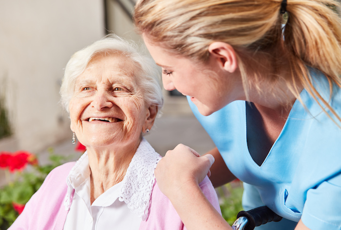 Fürsorgliche Altenpflegerin kümmert sich um Senior Frau im Rollstuhl im Pflegeheim